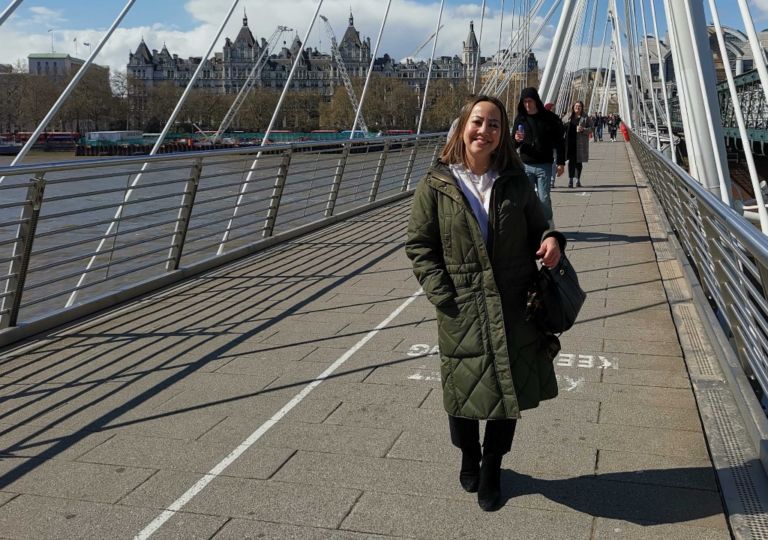 Kvinne med kåpe poserer på bro i London
