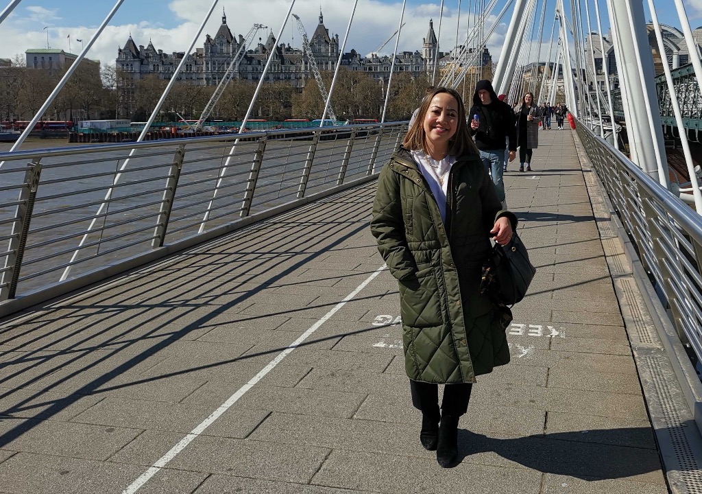Kvinne med kåpe poserer på bro i London